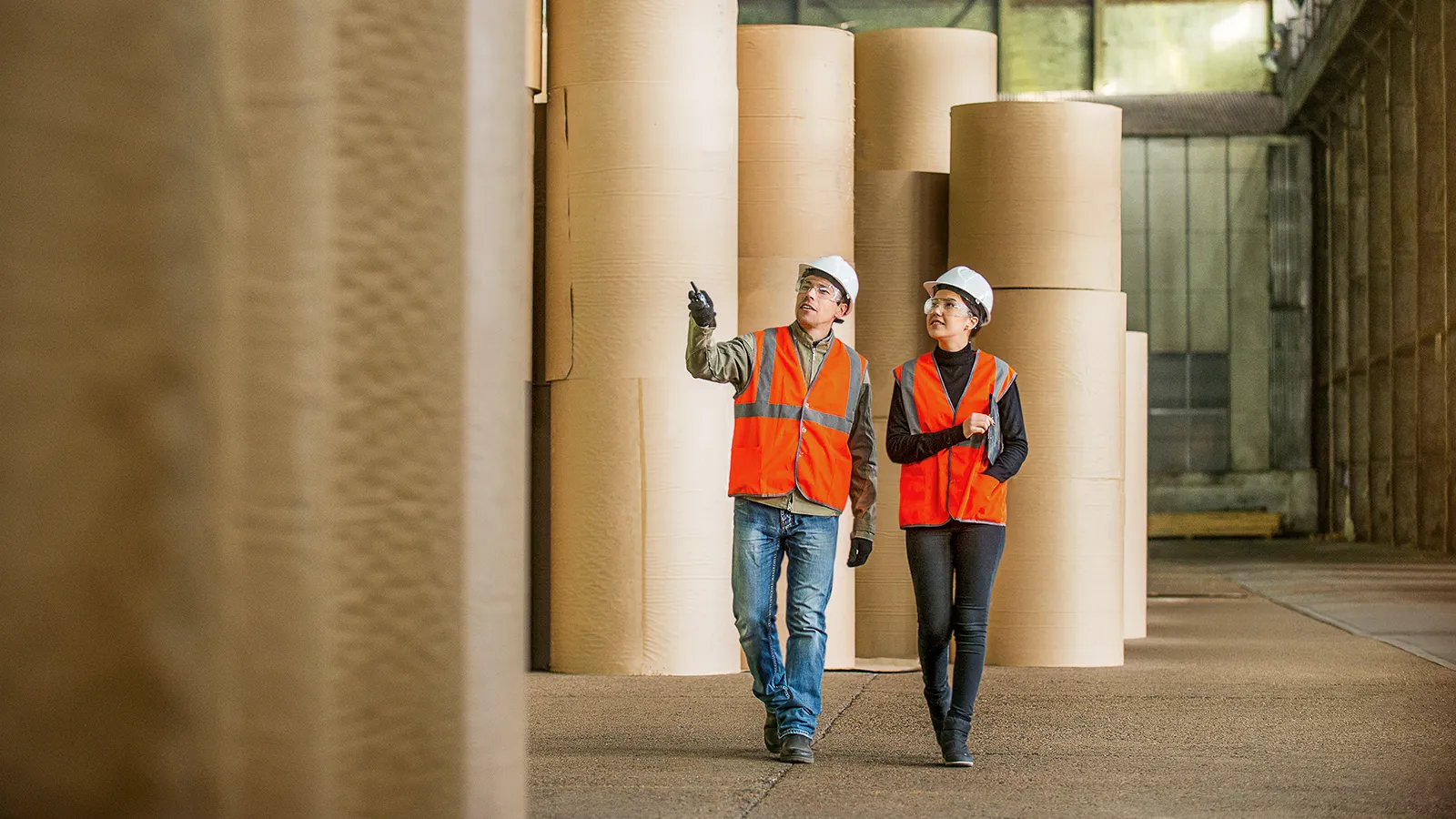 Man and woman in protective vests walk through a paper warehouse